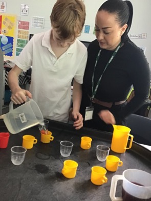 Student pouring drinks, helped by staff member